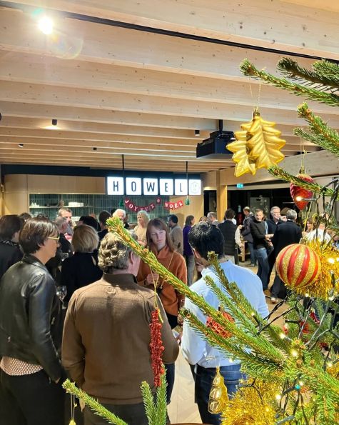 Soirée de Noël conviviale chez Howell, avec des collaborateurs échangeant dans une ambiance festive autour d'un sapin décoré.